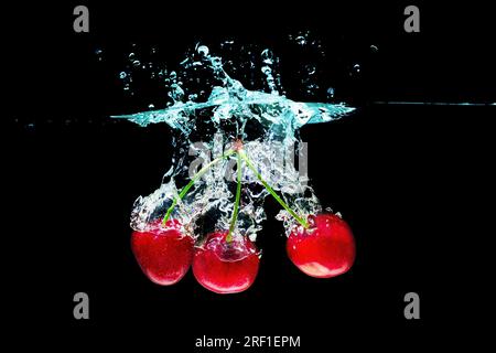 Close-up of three juicy sweet cherries dropped underwater with splashes isolated on black background. Stock Photo