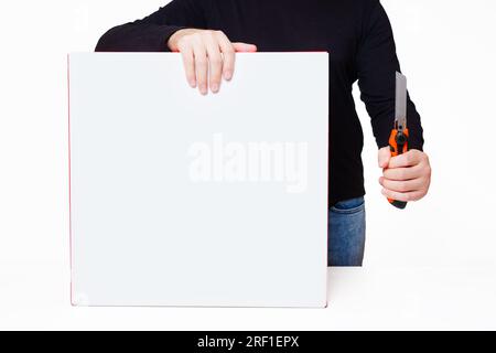 Person placing one hand on a large white box while holding a utility knife with a sizable blade in the other hand. Unboxing excitement related concept Stock Photo