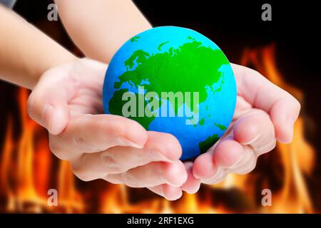 Blue and green model of the Earth held in hands against a backdrop of flames. Concept of environmental activism and the need for immediate action. Stock Photo