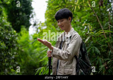 A happy and active young Asian male hiker using a compass while hiking in the forest. summer activity, hiking, trekking Stock Photo