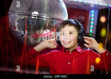 A young boy in headphones listens to music on the background of a disco ball. Stock Photo