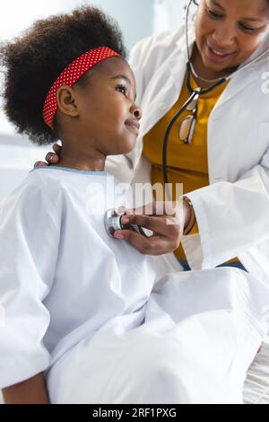 African american female doctor examining girl patient using stethoscope at hospital Stock Photo