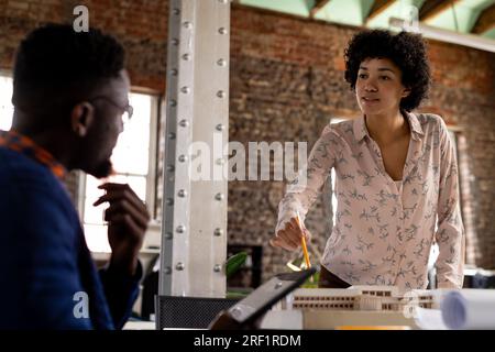 Diverse male and female architects discussing building model and using tablet at office Stock Photo