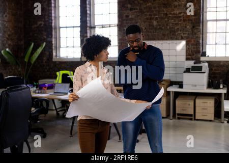 Diverse male and female architects discussing blueprints standing in office Stock Photo