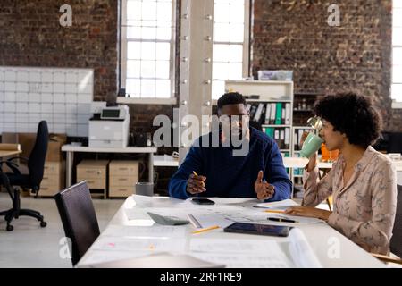 Diverse male and female architects having coffee discussing blueprints at desk in office, copy space Stock Photo