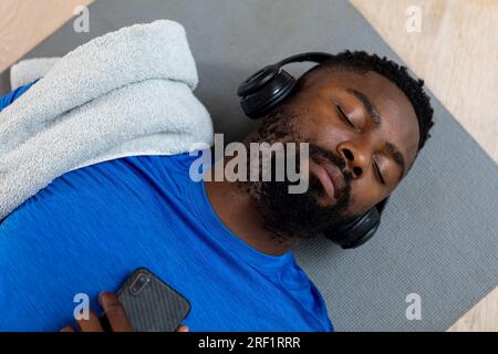African american man with headphones and smartphone lying on mat at home Stock Photo