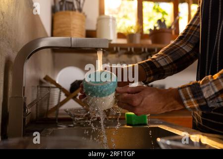 Midsection of indian man washing dishes in sunny kitchen at home Stock Photo