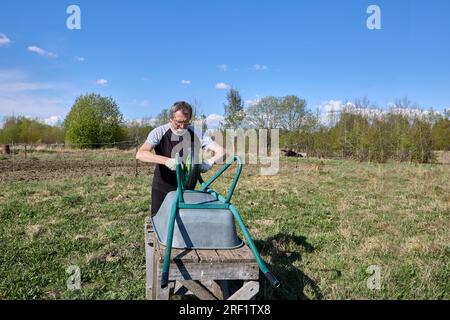 An elderly farmer repairs garden cart outdoors. Stock Photo