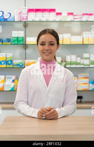 Young female pharmacist looking to the camera with products on the background Stock Photo