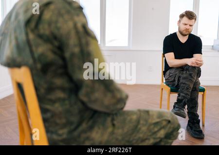 Cropped shot of unrecognizable male soldiers camouflage uniform talking sitting in circle during PTSD group therapy session. Concept of mental health Stock Photo
