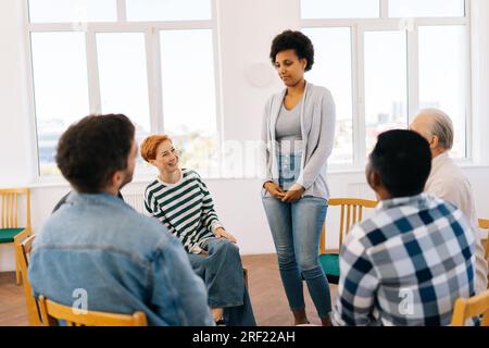 Portrait of African black female patient having breakthrough in group therapy session, standing by diverse and different ages sitting in circle. Stock Photo