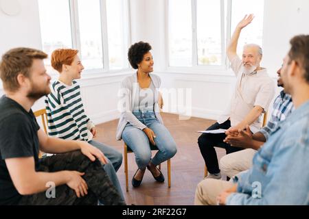 Group of diverse group of people sitting together in circle and raising hands in middle after therapy for high five. Smiling support group celebrating Stock Photo