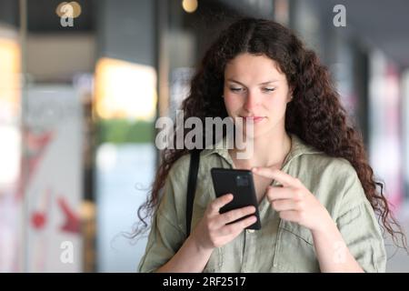 Woman checking phone walking in the street Stock Photo