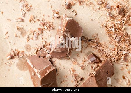 pieces of chocolate randomly scattered on the table, broken and crumbled natural chocolate, edible milk chocolate made from cocoa and sugar Stock Photo