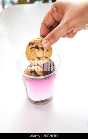 Assorted cookies in a plastic container to go cup, hand lifting one cookie out, sticker template placed for branding. Stock Photo