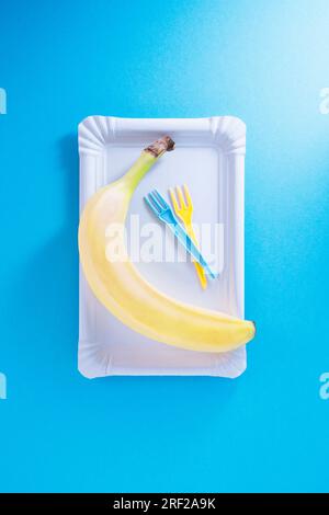 Banana on take-away plate against pale blue Stock Photo