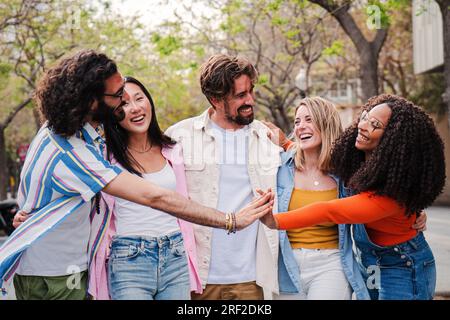 Group of happy friends having fun and laughing together outside, hanging each other showing complicity and friendship. Multiracial people enjoying free time socializing walking in city street together. High quality photo Stock Photo