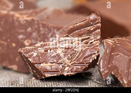broken and crumbled natural chocolate, edible milk chocolate made from cocoa and sugar, pieces of chocolate randomly scattered on the table Stock Photo
