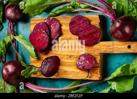 Fresh organic beetroot with green leaves on a vintage wooden cutting board on a blue background. Top view, copy space. Stock Photo
