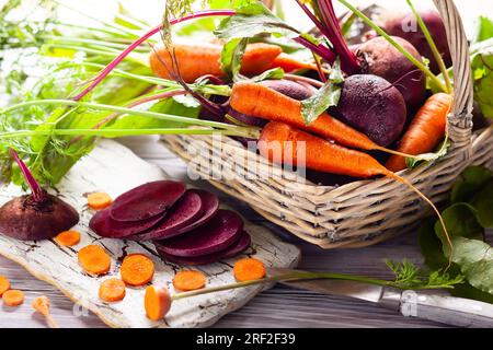 Fresh organic beetroot and carrot with green leaves in a basket on a  wnite wooden table. Stock Photo