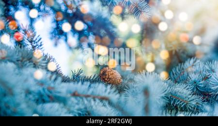 Christmas tree and lights bokeh around. New Year holidays concept with fir branches and pine cone on light background Stock Photo