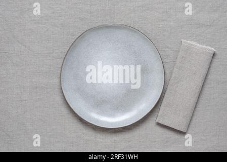 Empty gray plate mockup with gray linen napkin on gray linen background. Top view, flat lay, copy space. Stock Photo