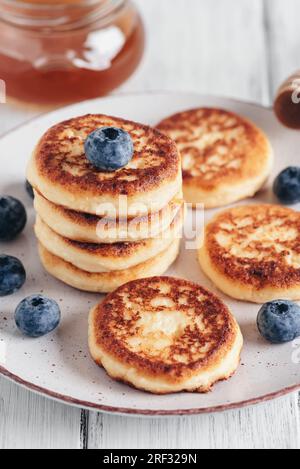 Homemade cottage cheese pancakes with blueberries and honey, white wooden old table. Side view, selective focus. Vertical image. Stock Photo