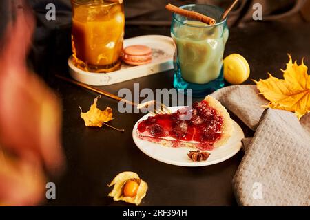 Atmospheric glass of pumpkin latte, cinnamon sticks and cherry pie. Seasonal autumn coffee time. Cozy home aesthetic. Stock Photo