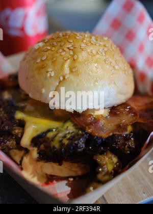 Double bacon cheeseburger served on a red & white checked napkin in a to go basket. Stock Photo