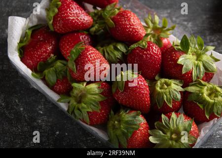 photo of many juicy, fresh, ripe strawberries in a plastic container, top view, vertical photo on a gray background Stock Photo