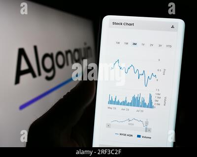 Person holding cellphone with website of Canadian company Algonquin Power Utilities Corp. on screen with logo. Focus on center of phone display. Stock Photo
