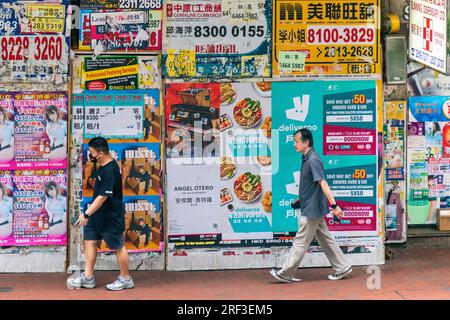 People walking past real estate and advertising posters on city centre wall, Hong Kong, SAR, China Stock Photo