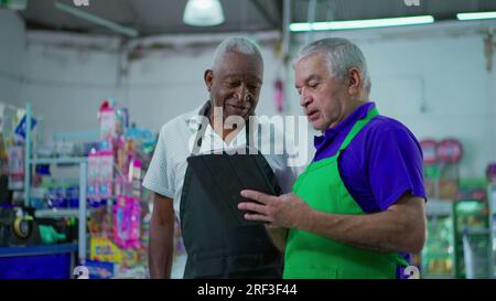 Two happy diverse senior staff of frocery store checking inventory operations with tablet device, older employees of supermarket laughing and smiling Stock Photo