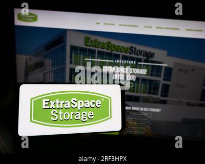 Person holding smartphone with logo of US company Extra Space Storage Inc. on screen in front of website. Focus on phone display. Stock Photo