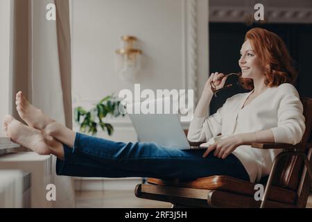 Content freelancer works comfortably from home, researching on social media, chatting online, and using her home internet connection. Stock Photo