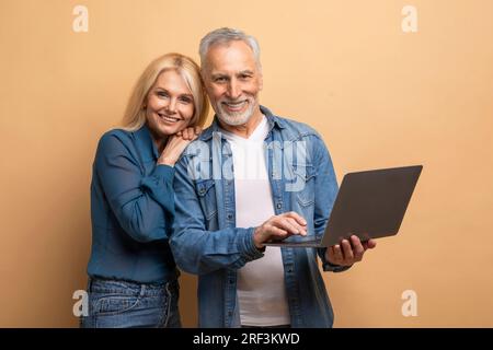 Loving elderly spouses using computer laptop on beige background Stock Photo