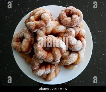 Freshly made sugar donuts piled on a white dinner plate on a black granite surface Stock Photo