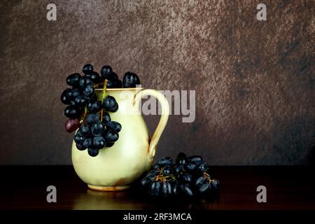 Old earthenware wine jug with bunches of grapes on a wooden table top Stock Photo