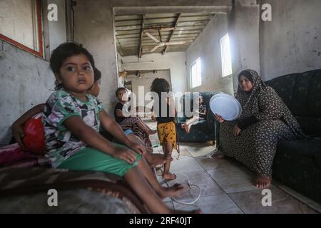 Gaza City, Palestinian Territories. 31st July, 2023. A Palestinian woman uses a plastic lid to cool off as she sits with her children inside her family's rudimentary home made of iron sheets, amid soaring temperatures and power outages in Gaza. The slums of Gaza suffer from deteriorating living conditions amid a growing electricity crisis, with normal power supplies only available for a few hours a day. Credit: Mohammed Talatene/dpa/Alamy Live News Stock Photo