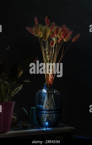 Some dried flowers in a blue glass vase that gets a ray of sun and goes through it Stock Photo