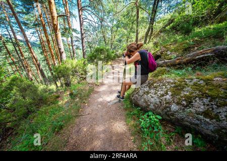 Woman hiker very tired and sitting on a rock on the road in the forest of Guadarrama, Madrid. Stock Photo