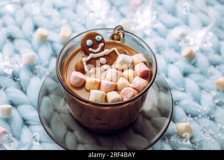 Gingerbread man soaking in a cup of hot chocolate with marshmallows, cozy winter setting in home. Stock Photo