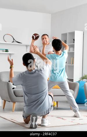Happy little boy with his dad and grandfather playing rugby at home Stock Photo