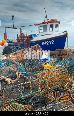 Traditional fishing boat pulled up onto the shingle beach at Aldeburgh with lobster pots stacked in front.  Suffolk, England, UK Stock Photo
