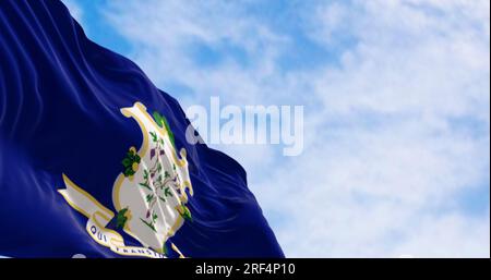 Connecticut state flag fluttering in the wind on a clear day. White shield on blue background featuring three grapevines each bearing bunches of grape Stock Photo