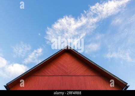 Red wooden gable is under blue cloudy sky on a daytime, rural Scandinavian architecture background Stock Photo