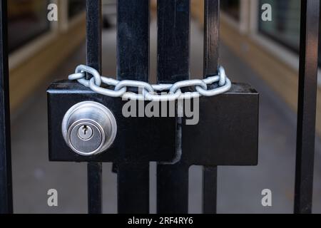 Lock and strong steel chain wrapped around the metal entrance gate. Closed metal gates with lock on an entrance black gate. Safety, security concept. Stock Photo