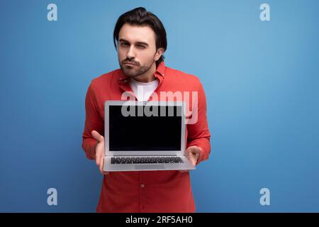 charming positive 30s man in red shirt showing laptop screen mockup Stock Photo