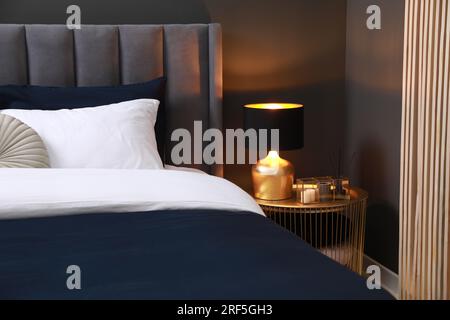 Comfortable bed with cushions, lamp and different decor on bedside table in room. Stylish interior Stock Photo