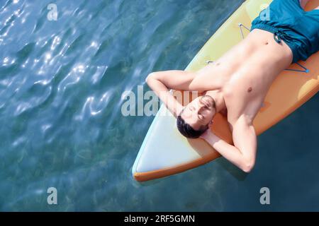 Man lying on SUP board in sea, top view. Space for text Stock Photo